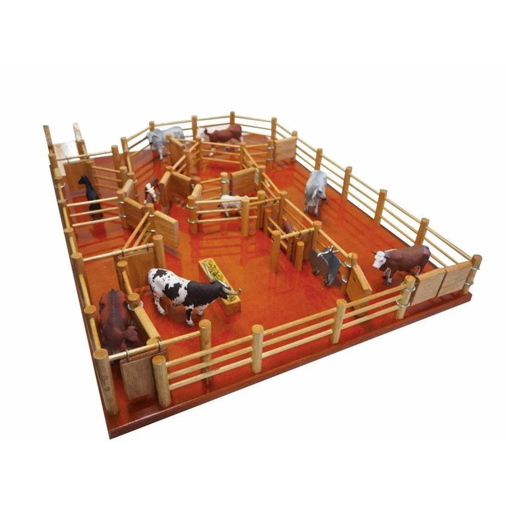 Country Toys CY8 Wooden Station Cattle Yard. Handmade wooden toy cattle yard with multiple gates, feed trough, water trough, and a metal branding cradle, displayed on a red surface.