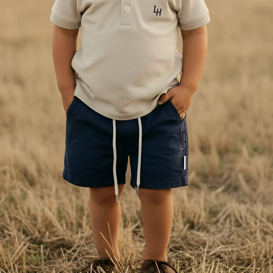 Child wearing a beige polo shirt and navy shorts standing in a field.