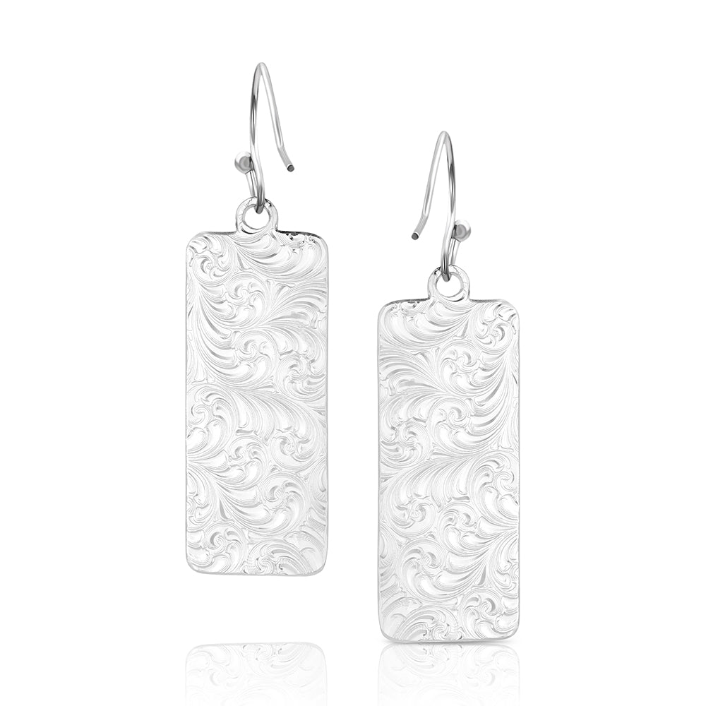 A pair of silver drop earrings featuring rectangular plates with an embossed scrollwork pattern, suspended from simple silver fishhook wires, shown against a plain white background.