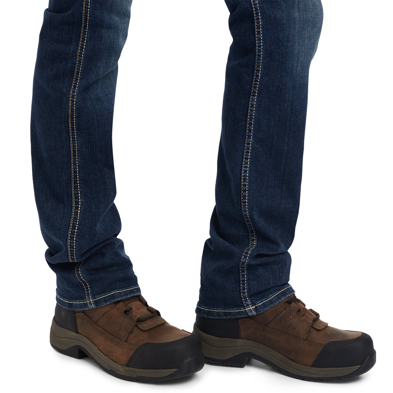 Brown shoes with black soles worn with blue jeans on a white background