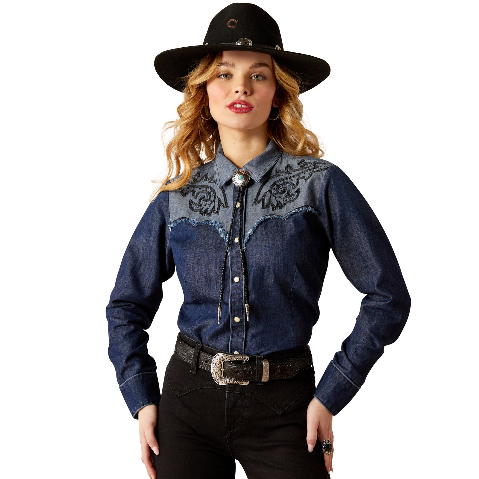 Ariat Women's Second Fiddle L/S Western Shirt. A woman wearing a blue long-sleeved Western shirt with embroidery on the chest, paired with black pants and a black cowboy hat.