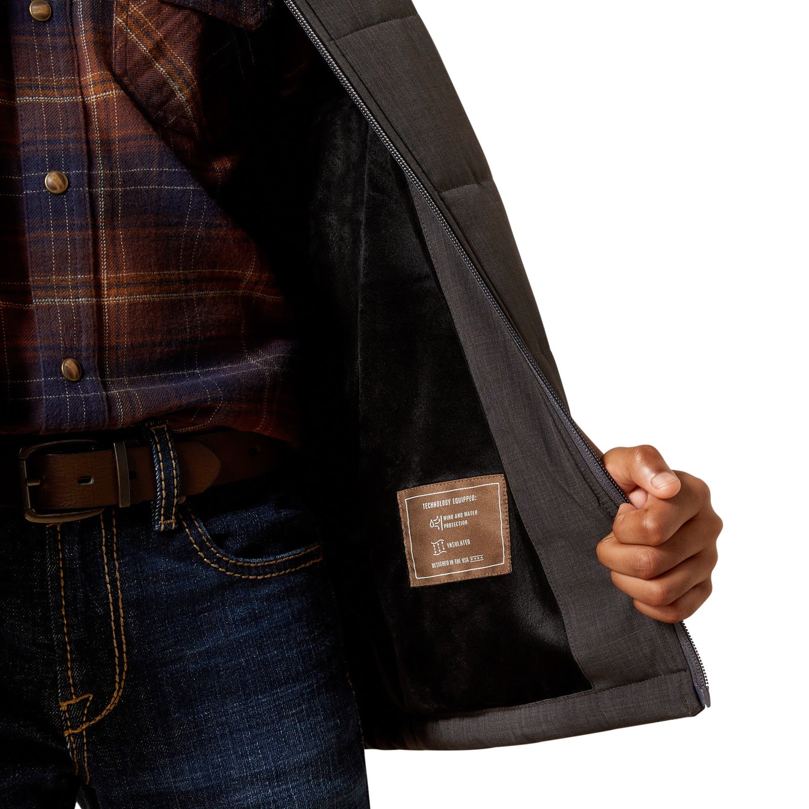 Close-up of a person wearing a plaid shirt and dark jacket with a visible brand label.