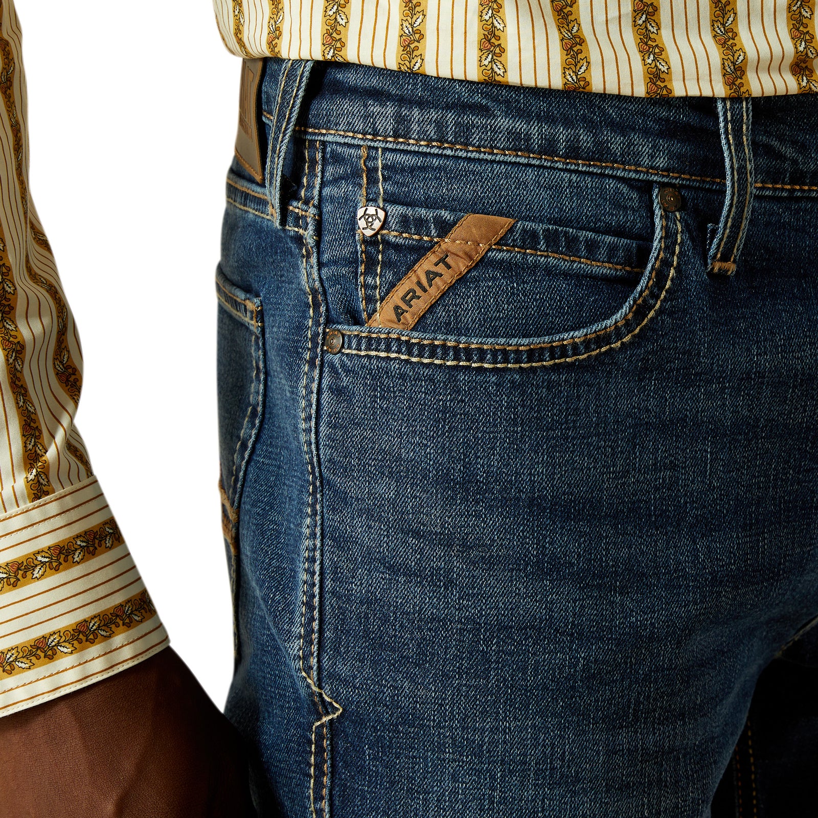 Ariat Men's Samuel M8 Straight Leg Jean. Close-up of blue jeans with a brand label, worn with a patterned shirt.