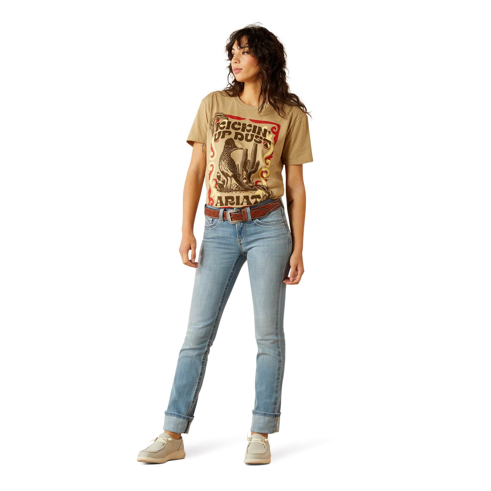 Ariat Women's Bessie Perfect Rise Slim Trouser. Woman wearing a graphic t-shirt and light blue jeans on a white background