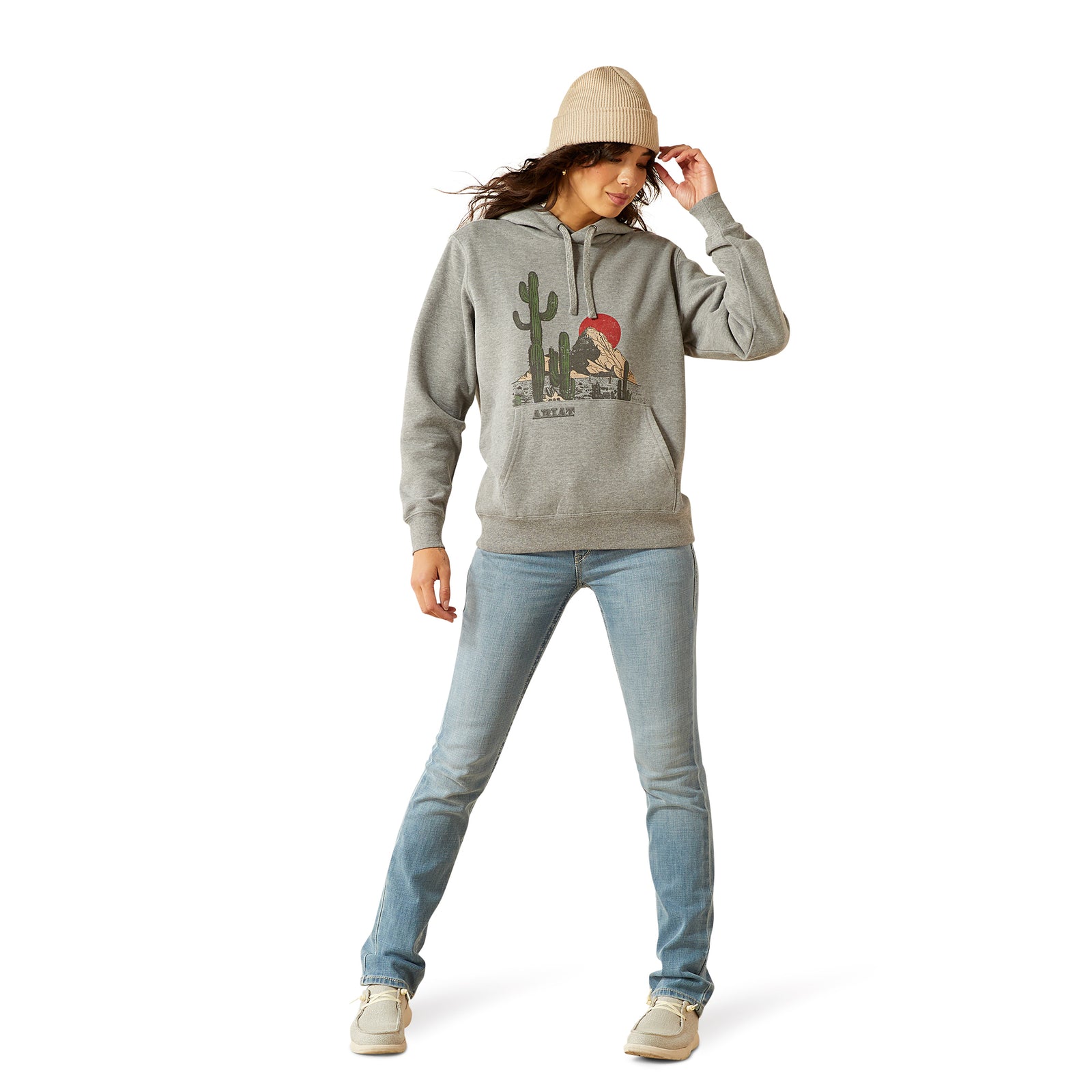 Person wearing a gray hoodie with a graphic design, light blue jeans, and beige beanie on a white background