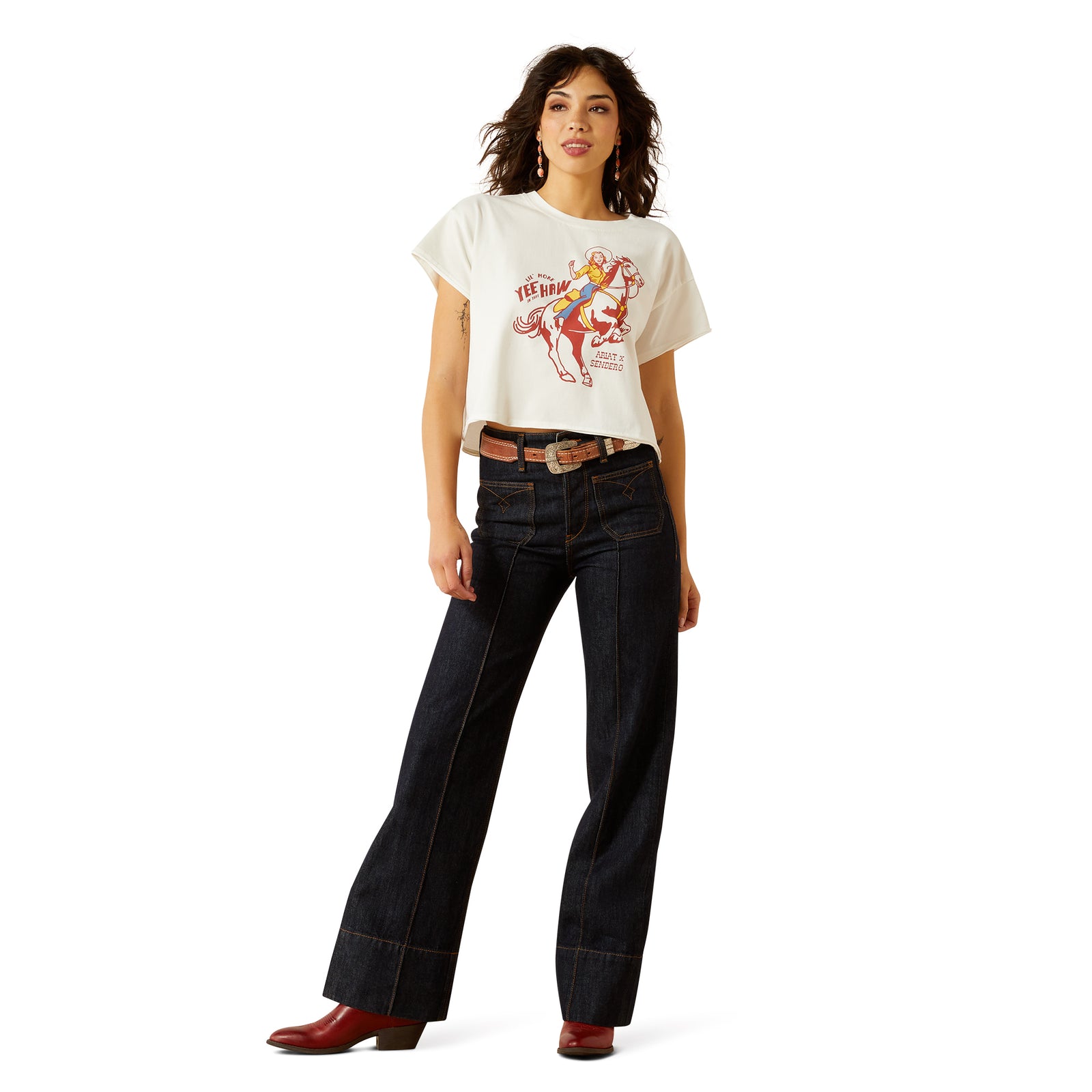 Ariat Women's Sendero Yeehaw S/S T-Shirt. Woman wearing a white t-shirt with a graphic design and dark jeans on a white background