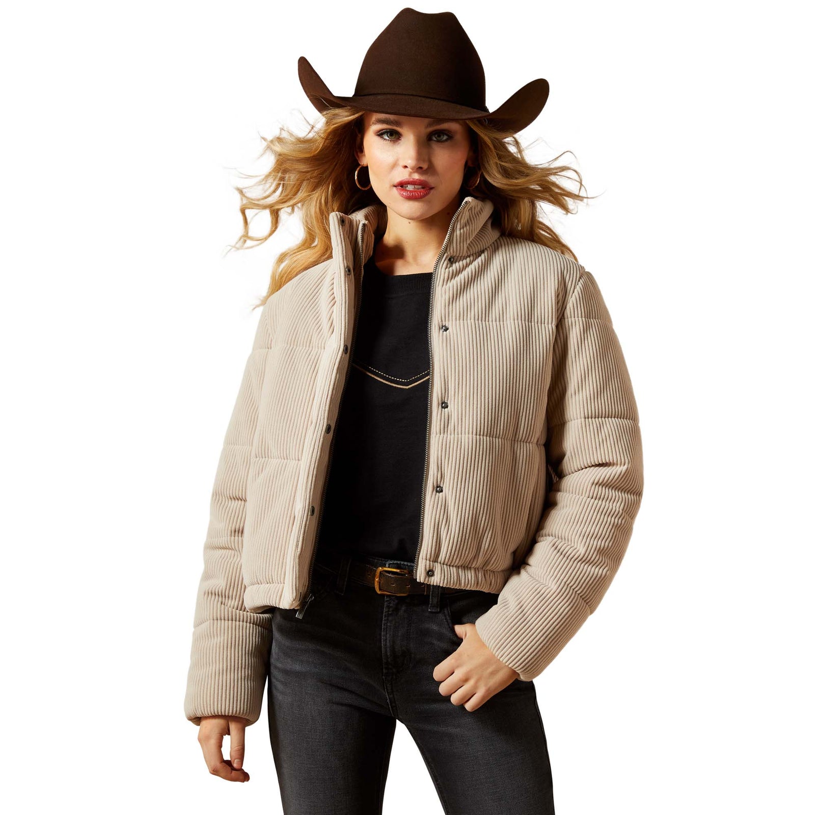 Woman wearing a beige puffer jacket, black top, dark jeans, and a brown cowboy hat on a white background
