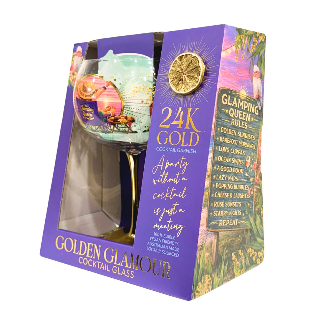 A boxed Golden Glamour 24K Gold Cocktail Glass shown at an angle. The packaging is predominantly purple with gold lettering, a lemon slice graphic, and a floral illustration on the side panel.