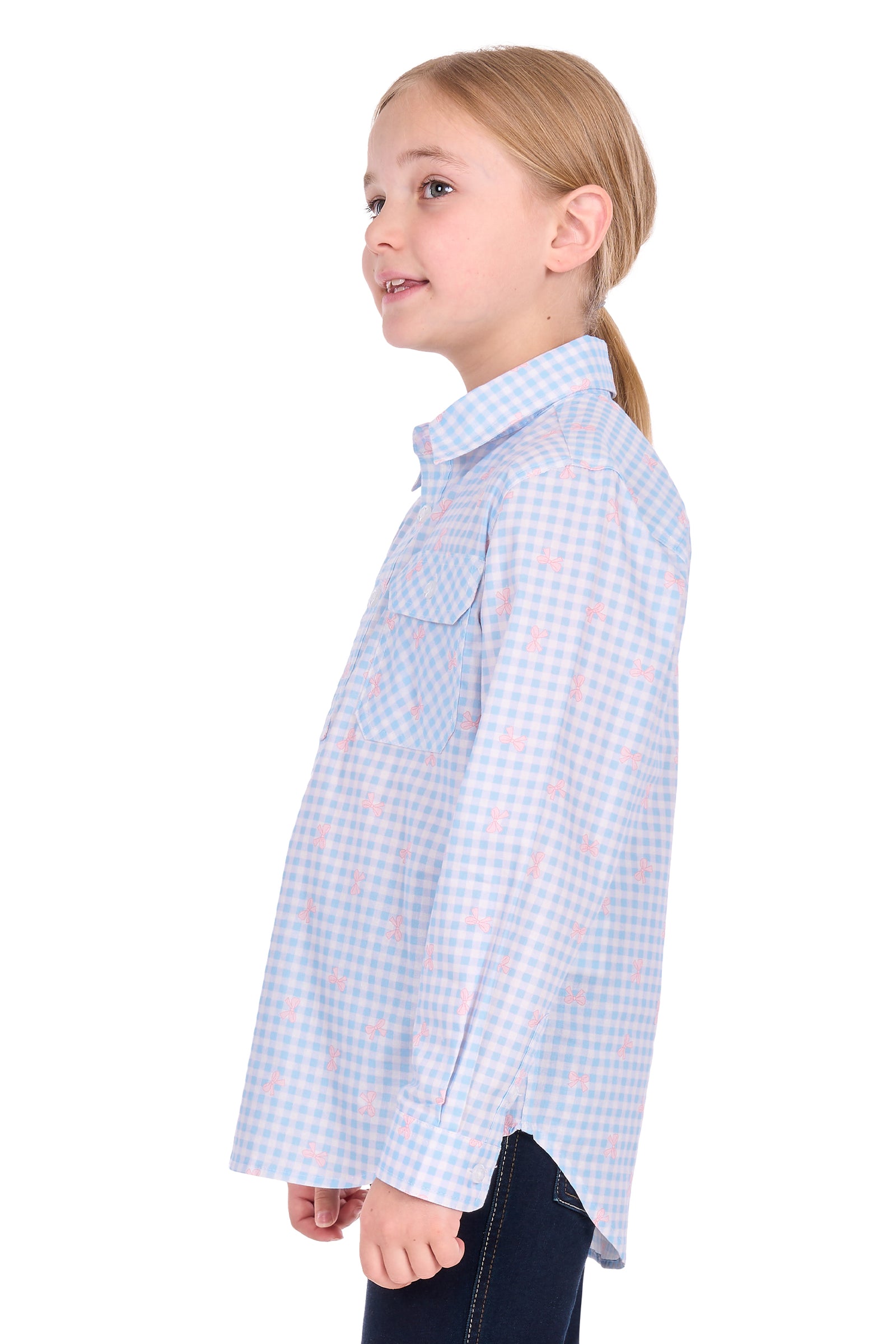 A young girl with blonde hair tied back in a ponytail is shown in profile wearing a light blue and white gingham long-sleeve button-up shirt with a pink gingham pattern, paired with dark blue jeans, against a solid white background.