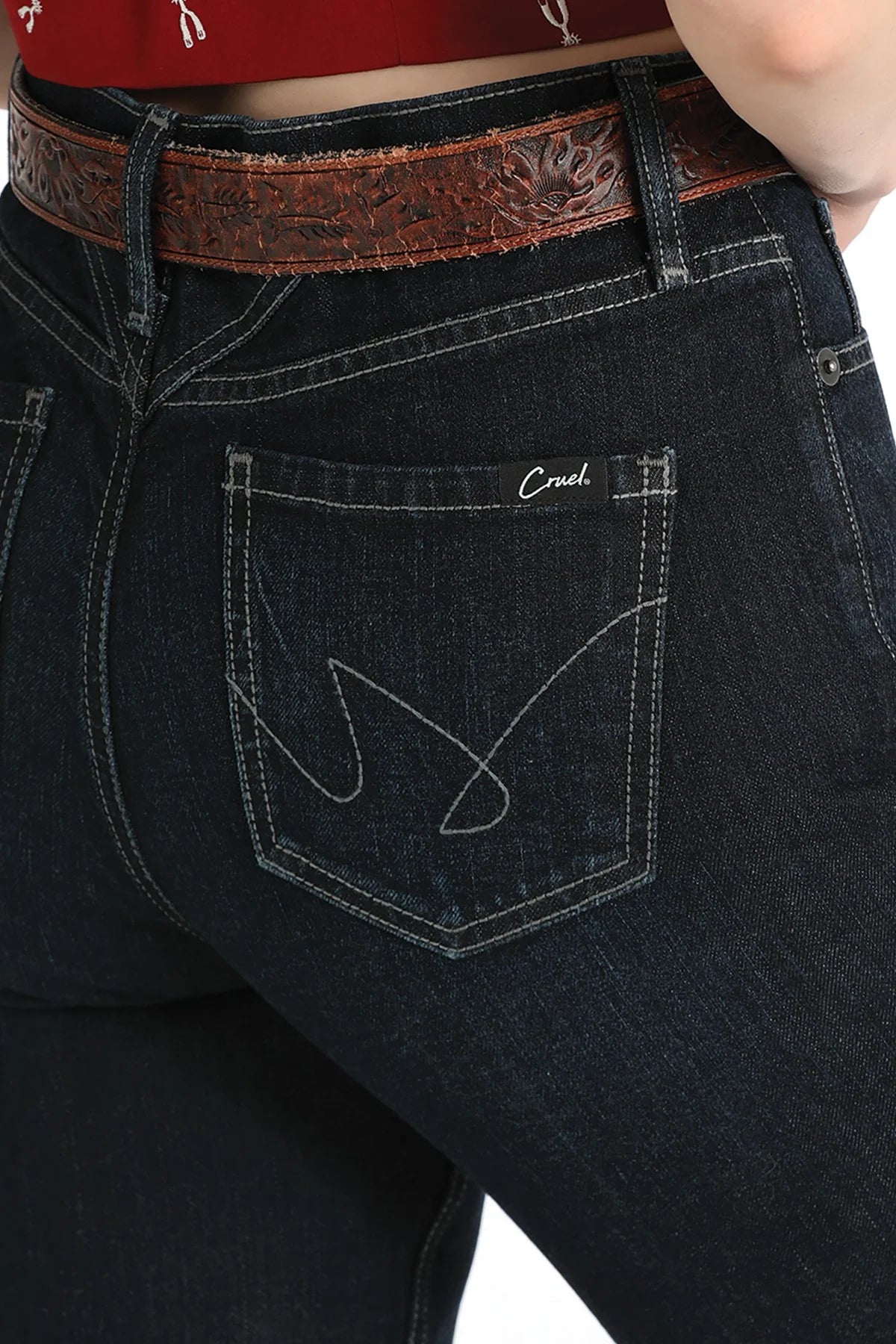 Close-up of the back pocket of dark wash denim jeans with white contrast stitching, a white embroidered 'Creek' logo, and a brown tooled leather belt.