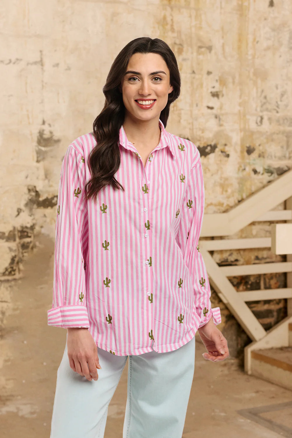 Woman wearing a pink striped shirt with cactus patterns in an outdoor setting.