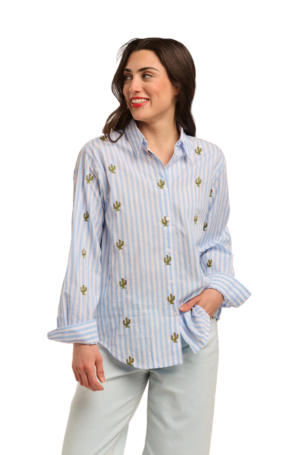 Italian Star Women's Stripe Cactus L/S Shirt. Woman wearing a light blue striped shirt with gold accents against a textured beige wall.