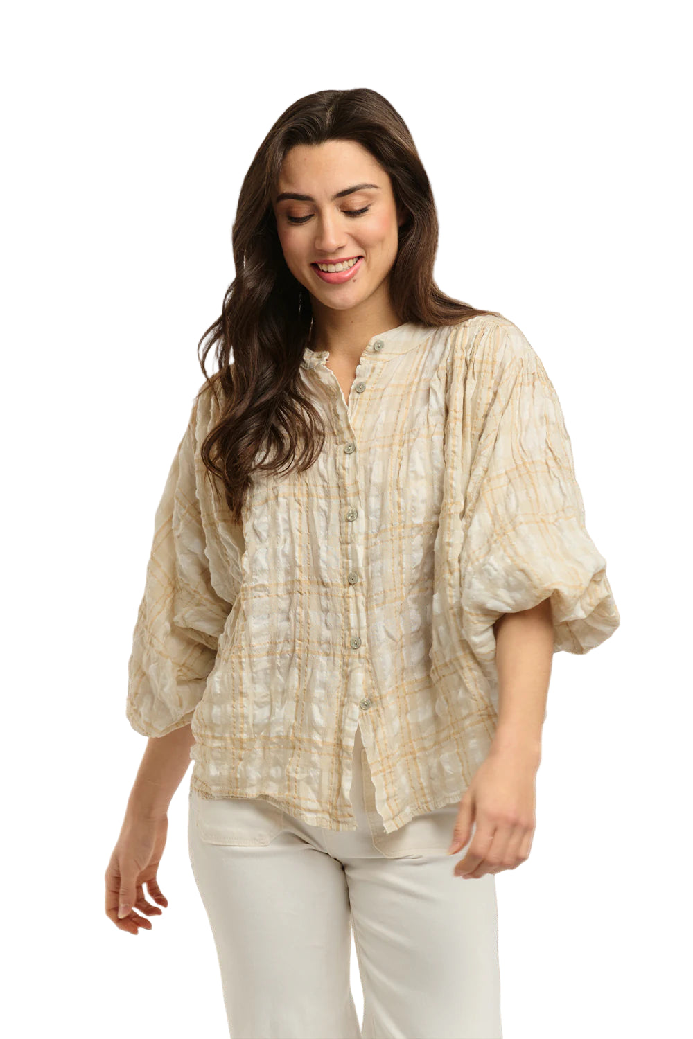 Italian Star Women's Freida Check Shirt. Woman wearing a patterned blouse and white pants standing against a stone wall.