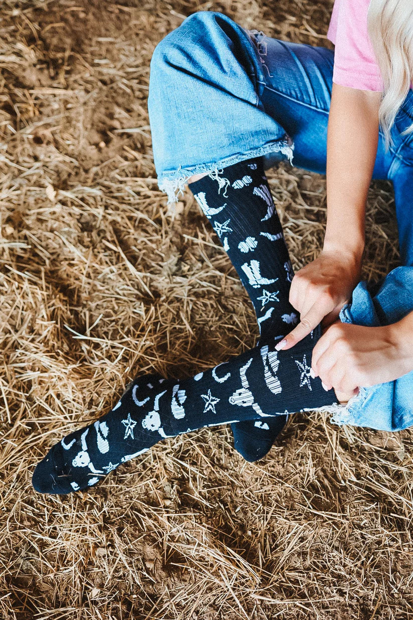 Lucky Chuck Get Western Performance Socks. Person wearing black socks with white patterns on a straw background