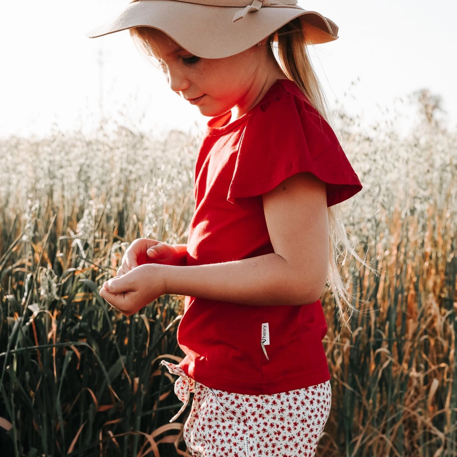 Love Henry Girl's Frill Sleeve Top. A girl wearing a red frill sleeve top standing in a field