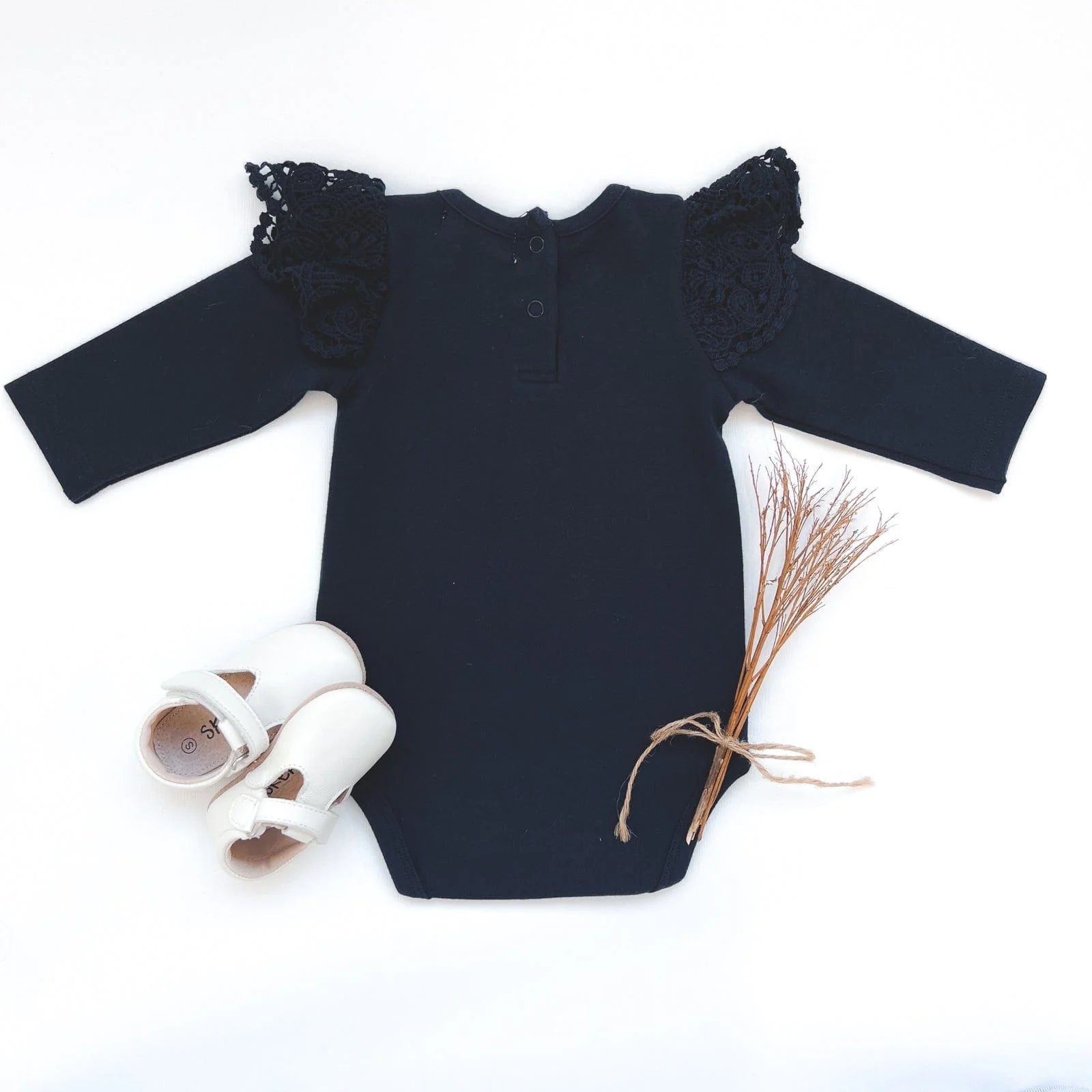 Love Henry Baby Girl's Lace Sleeve Onesie. Navy baby onesie with lace sleeves and a bias bound crew neck, accompanied by a pair of white shoes and a decorative element.