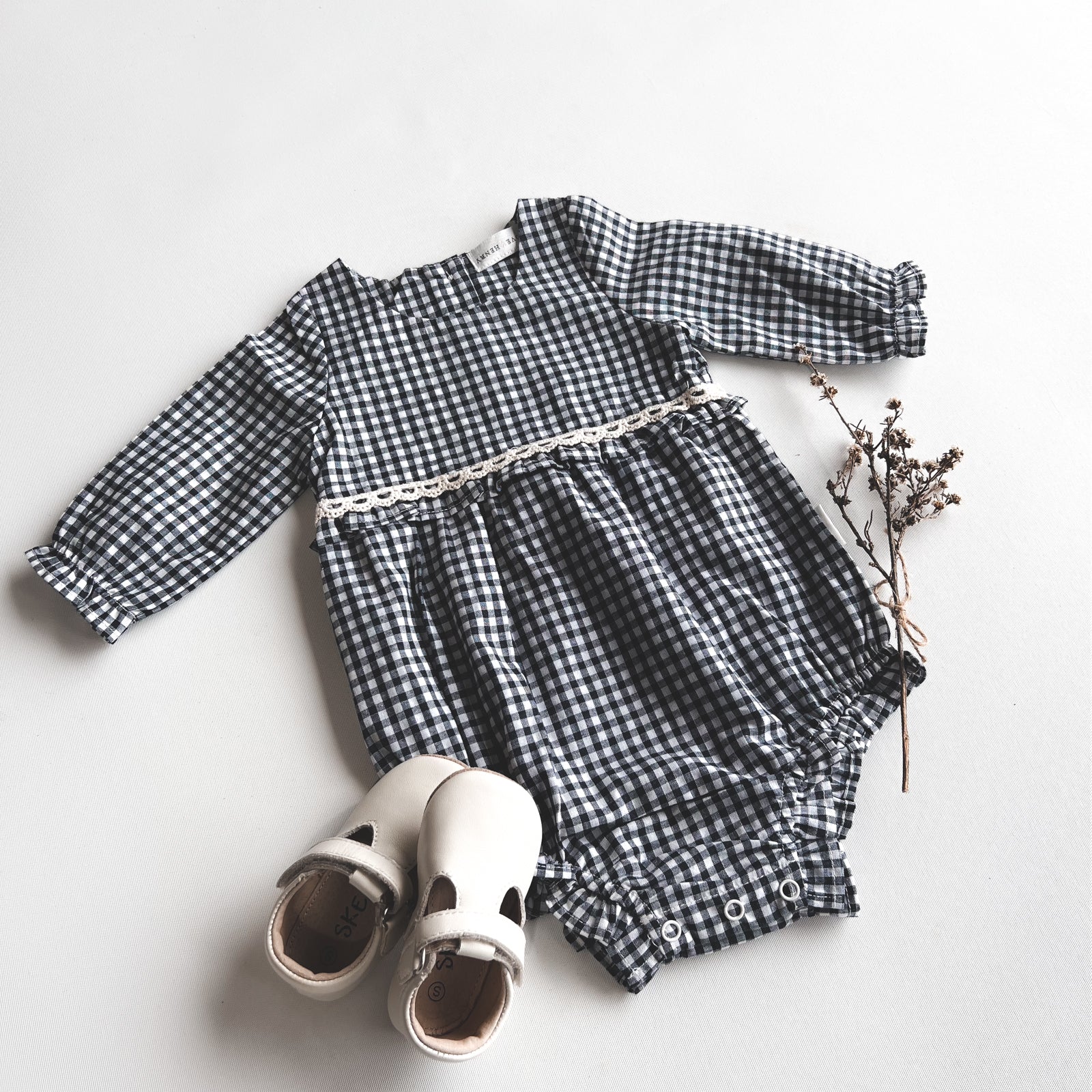 Love Henry Baby Girls L/S Nora Playsuit - Navy Check. Navy and white checkered baby romper with white shoes on a light gray background