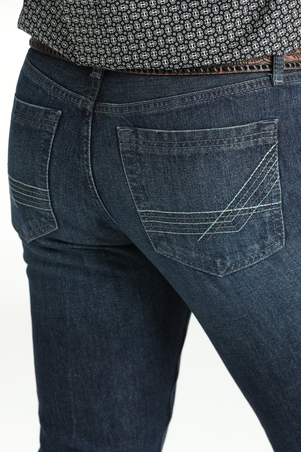 Cinch Men's Ian Dark Wash Slim Fit Jeans. Close-up of dark blue jeans with a patterned shirt underneath on a white background
