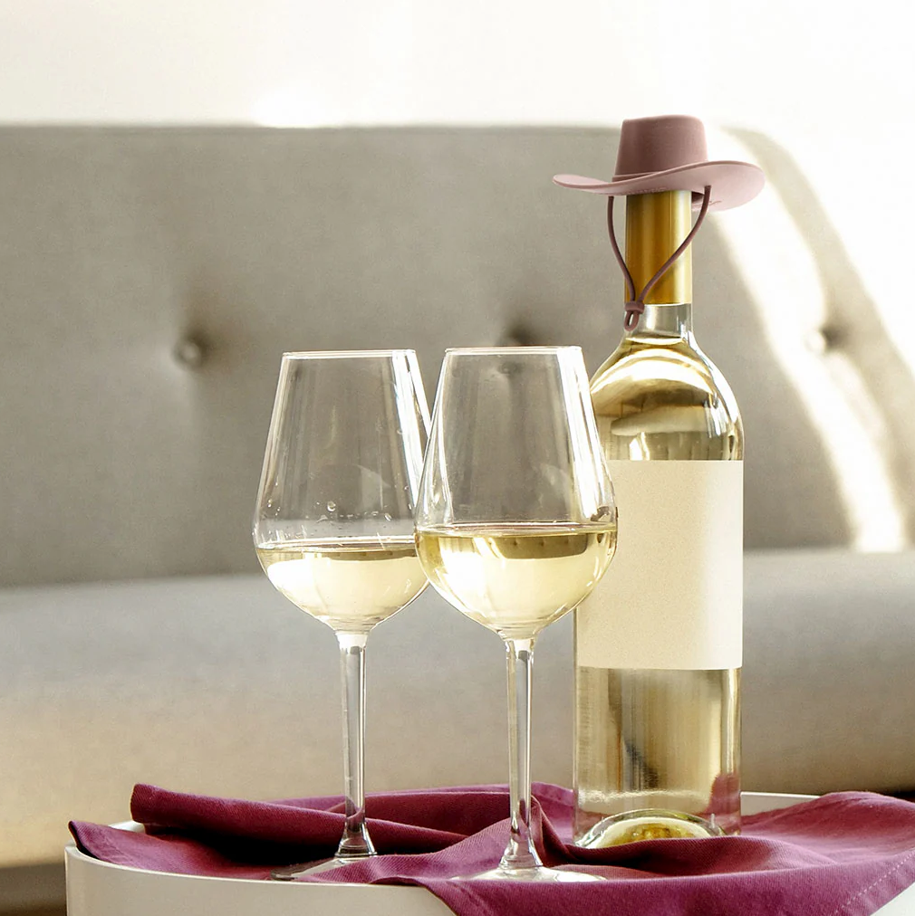 Monkey Business Howdy Bottle Stopper Set 2. Two wine glasses with white wine and a bottle of white wine on a table with a blurred background.