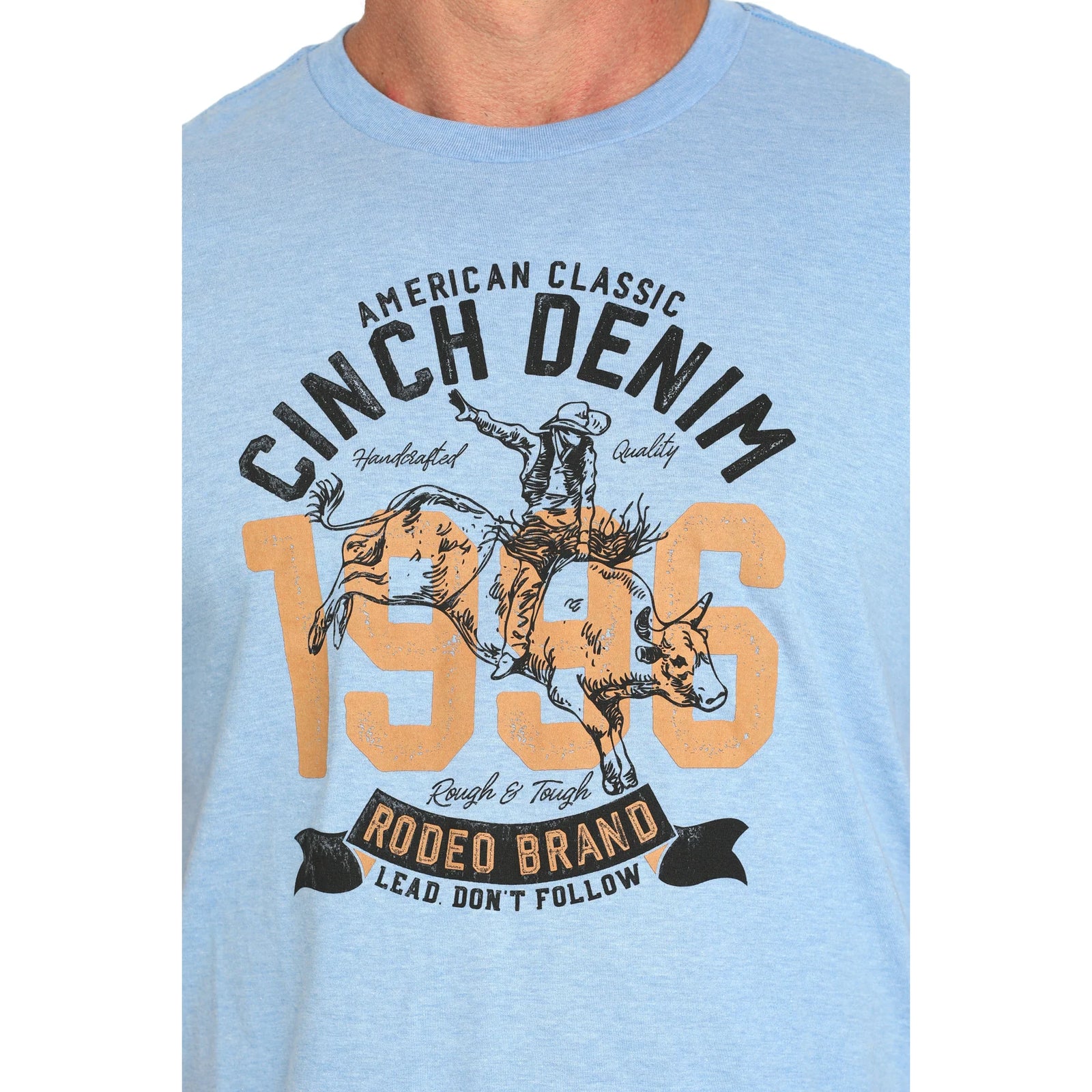 Cinch Men's Western Graphic T-Shirt. Light blue t-shirt with a graphic of a cowboy on a horse and text 'American Classic Cinch Denim 1946 Rodeo Brand'.