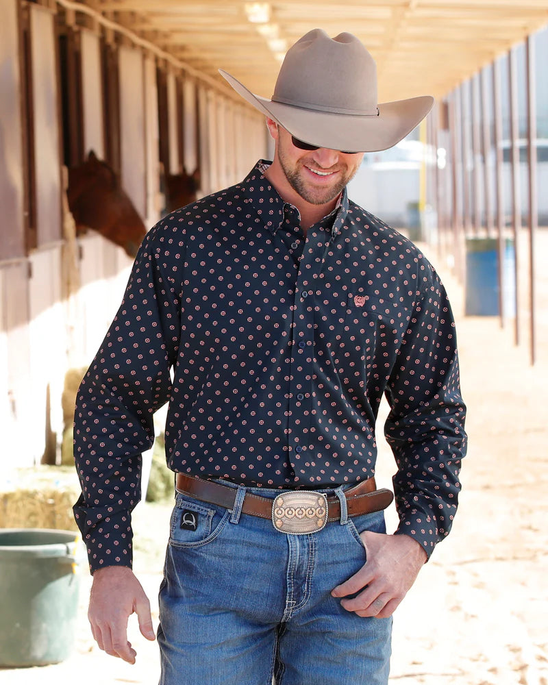 Man wearing a cowboy hat, patterned shirt, and jeans in an outdoor setting.