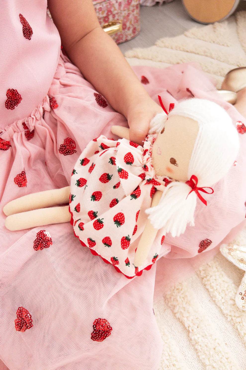 Child holding a plush toy with strawberry pattern on a pink blanket