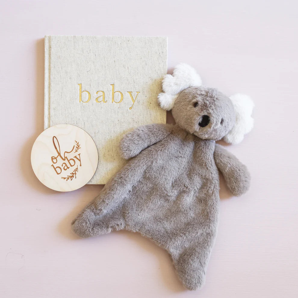 Gray teddy bear with a white bow and a book titled 'baby' on a light pink background.