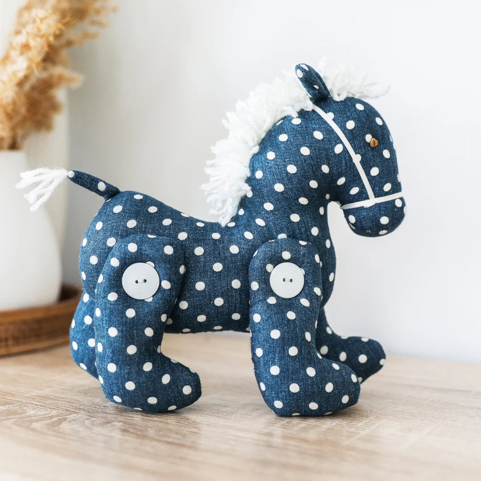 Blue polka dot horse toy on a wooden surface with a white background