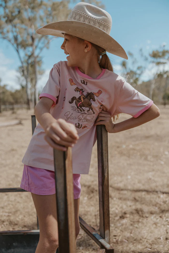 Person wearing a pink shirt with a horse graphic and pink shorts, standing outdoors.