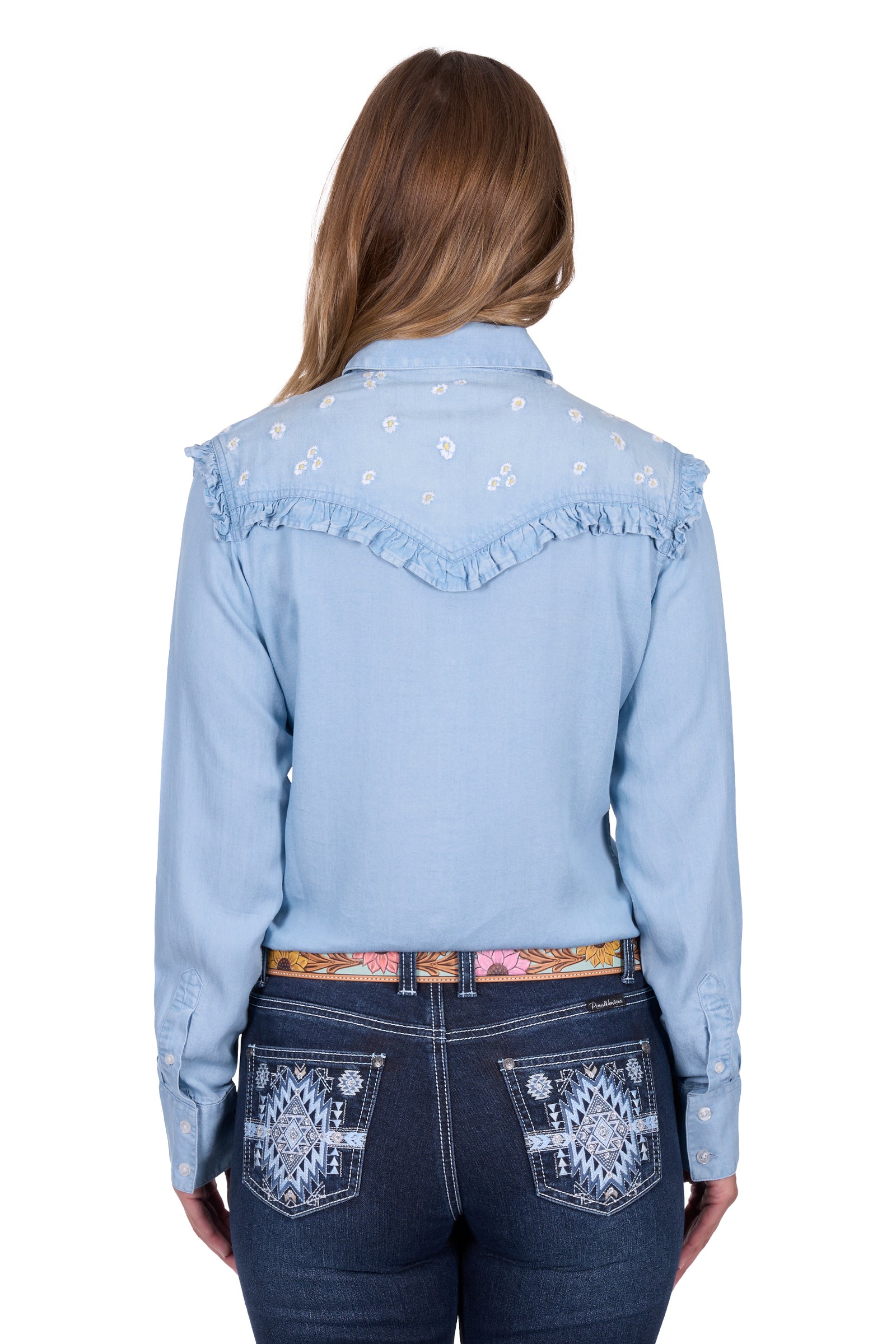 Pure Western Women's Phoebe L/S Western Shirt. Woman wearing a light blue denim shirt with floral embroidery and dark blue jeans on a white background