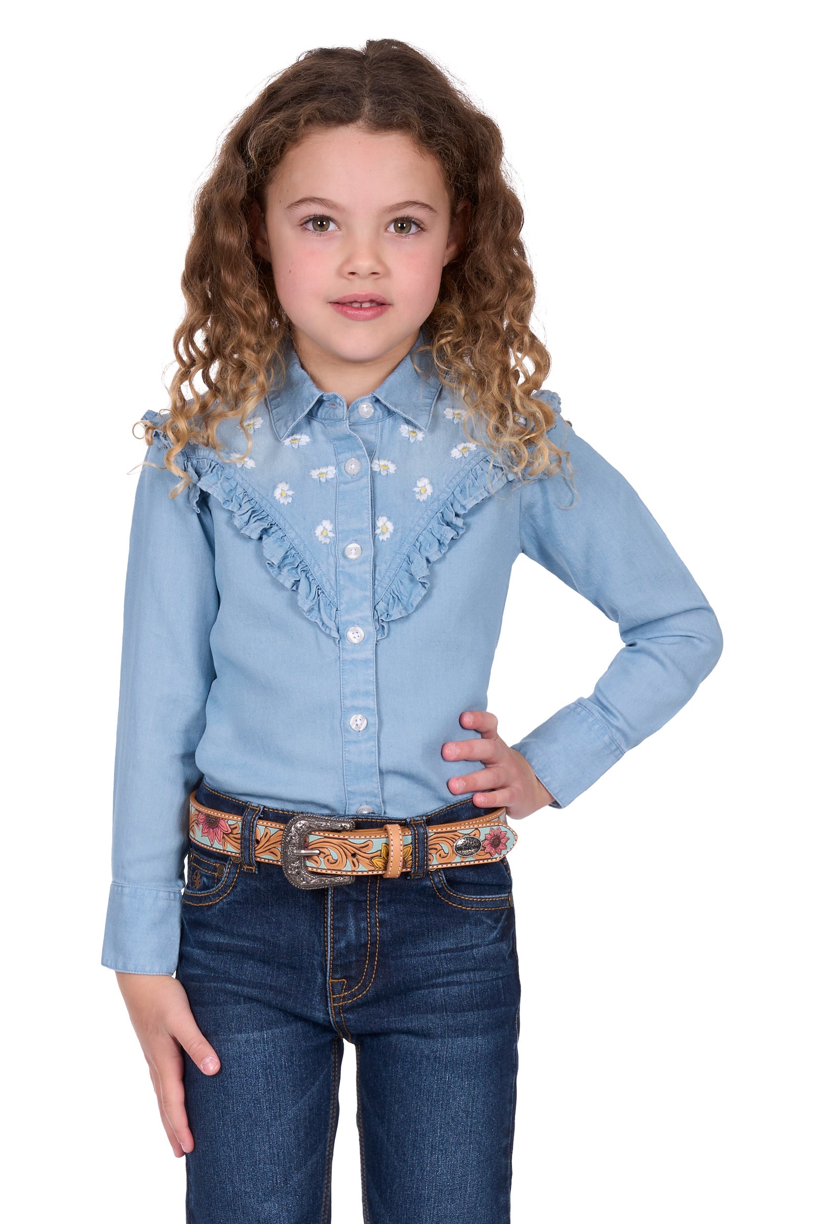 Pure Western Girl's Pheobe L/S Western Shirt. Young girl wearing a light blue denim shirt with ruffles and dark blue jeans on a white background