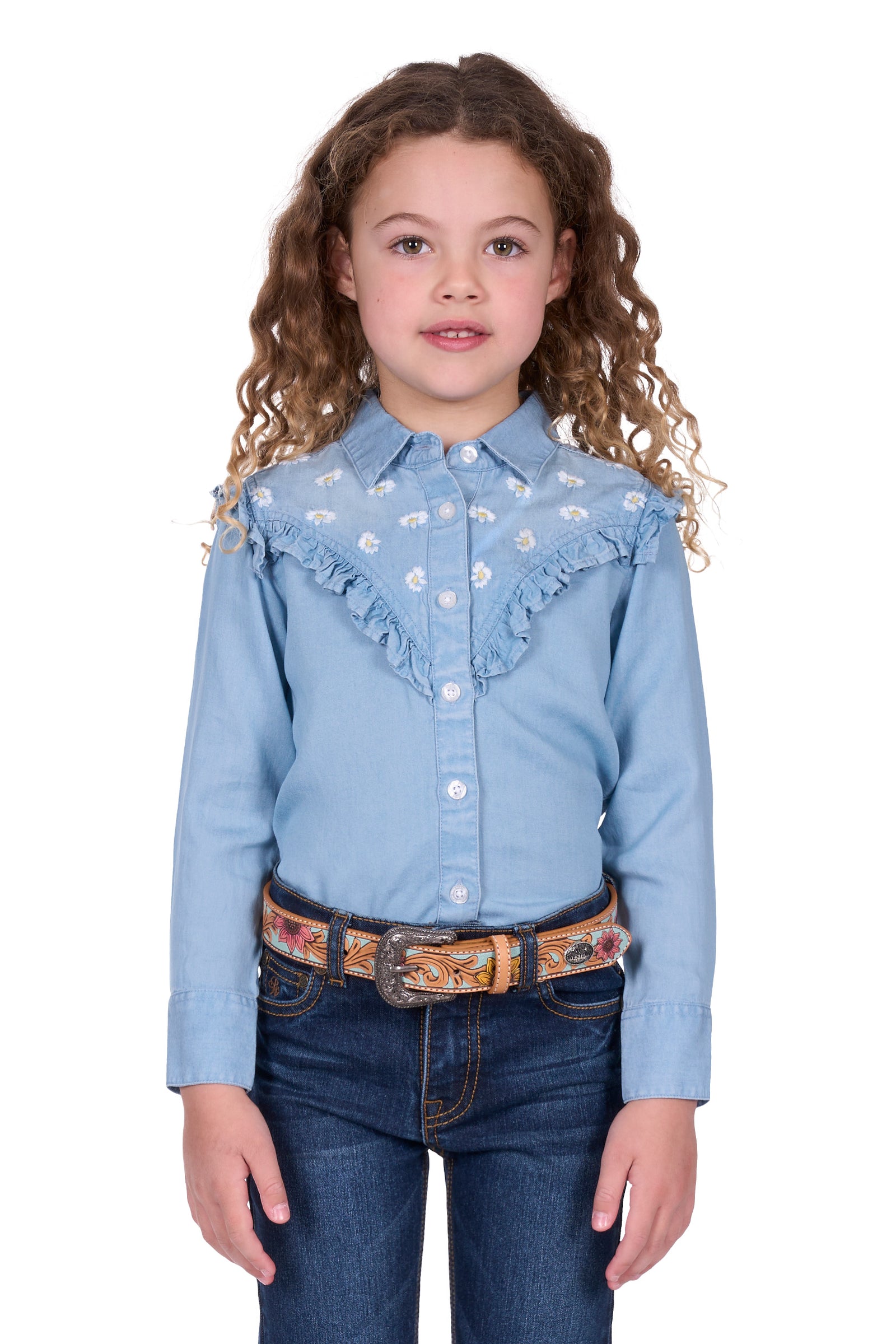 Pure Western Girl's Pheobe L/S Western Shirt. Young girl wearing a light blue denim shirt with ruffles and dark blue jeans on a white background