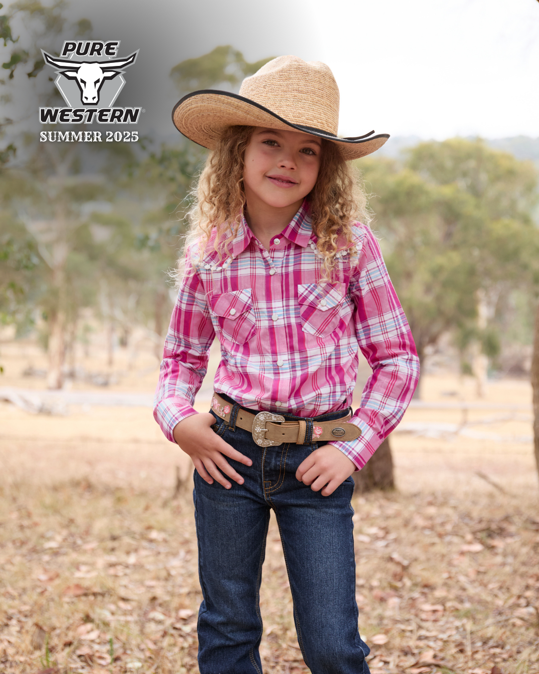 Pure Western Girl's Sam Boot Cut Jean. Child wearing a pink plaid shirt, blue jeans, and a straw cowboy hat with 'PURE WESTERN' branding.