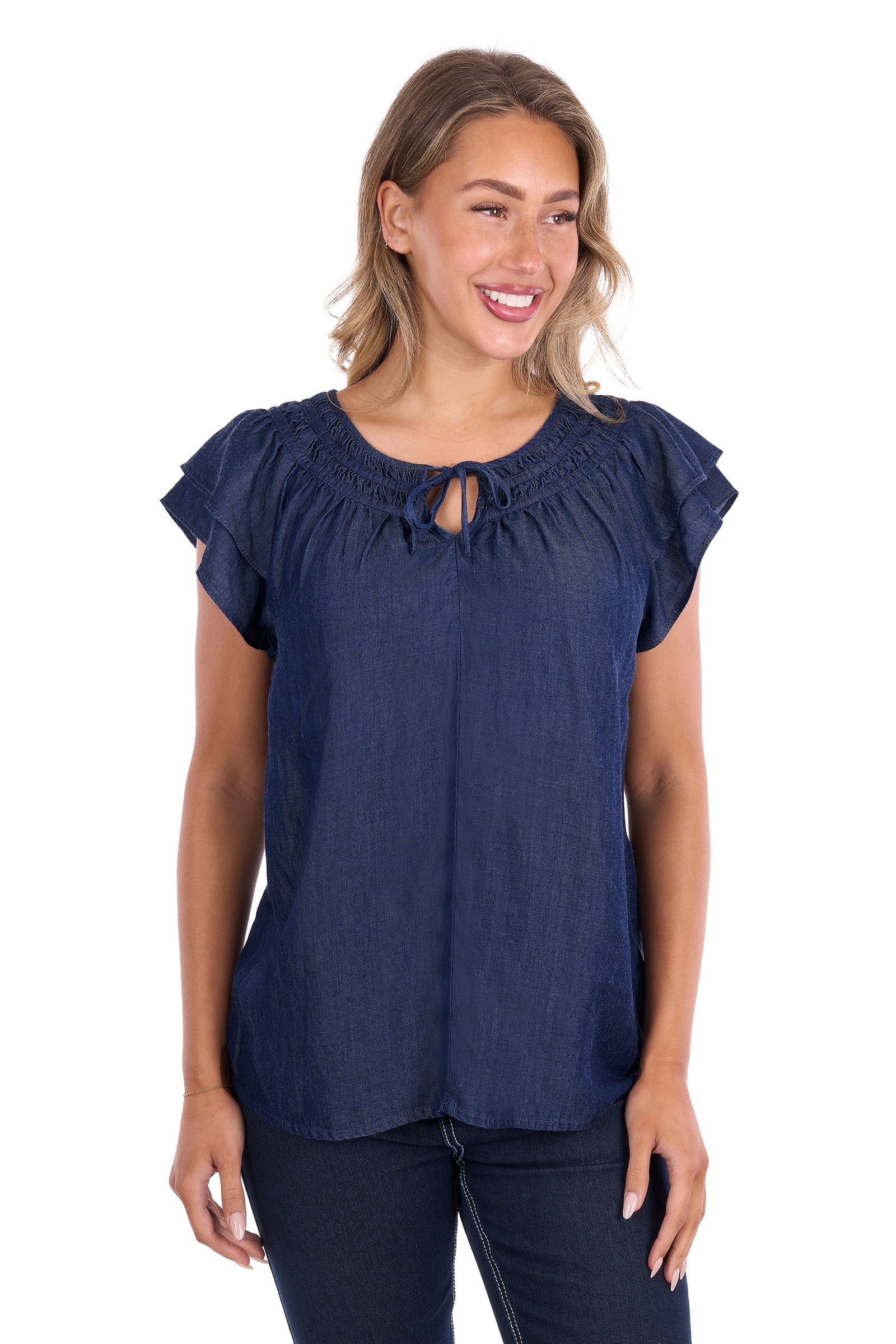 A woman wearing a navy blue short-sleeve top with a smocked round neckline and keyhole tie detail, paired with dark jeans, against a plain white background.