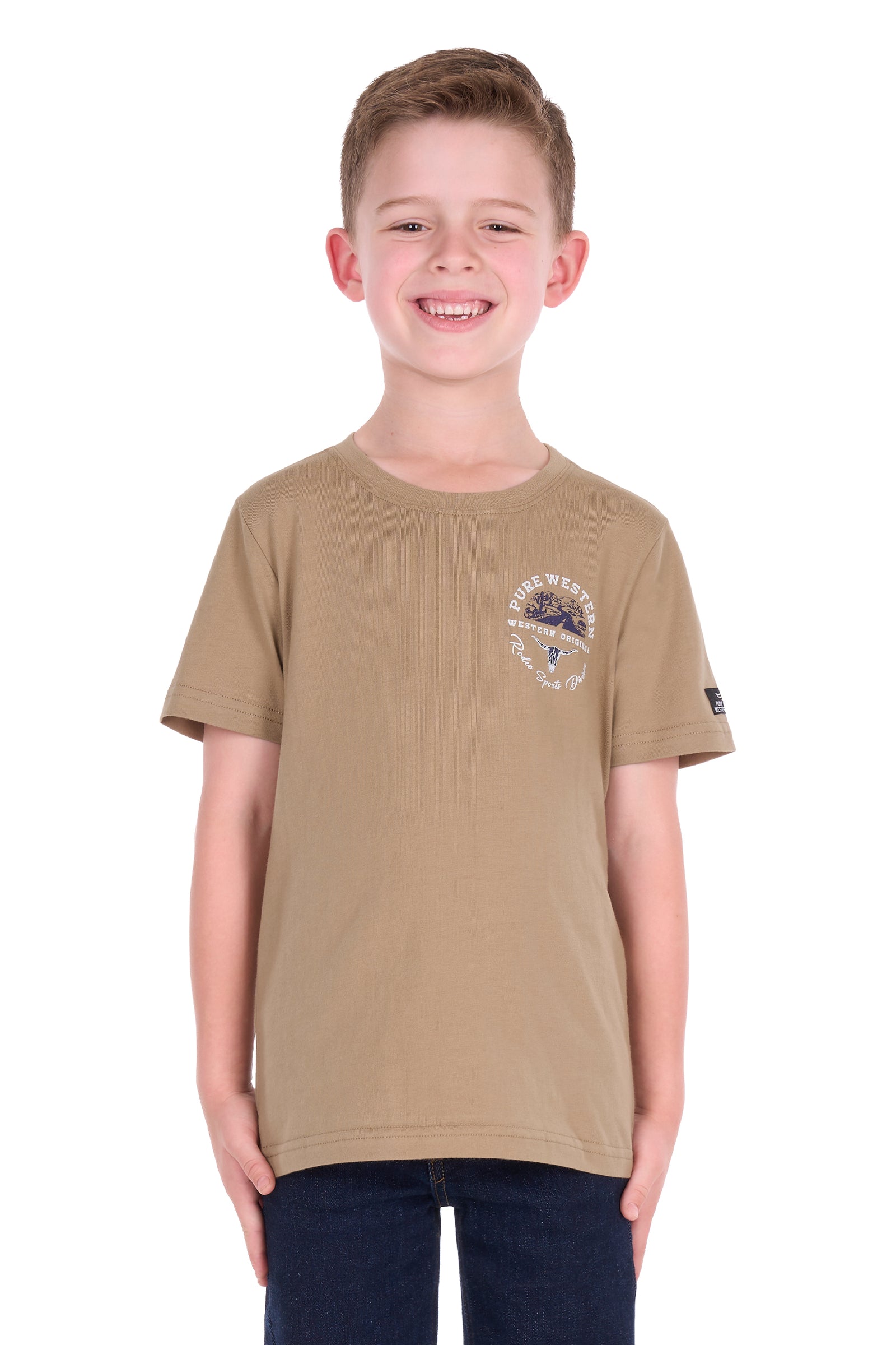 A young boy smiling, wearing a tan short-sleeve crewneck t-shirt with a small graphic on the left chest and a black brand patch on the right sleeve, paired with dark blue jeans, shot against a plain white background.