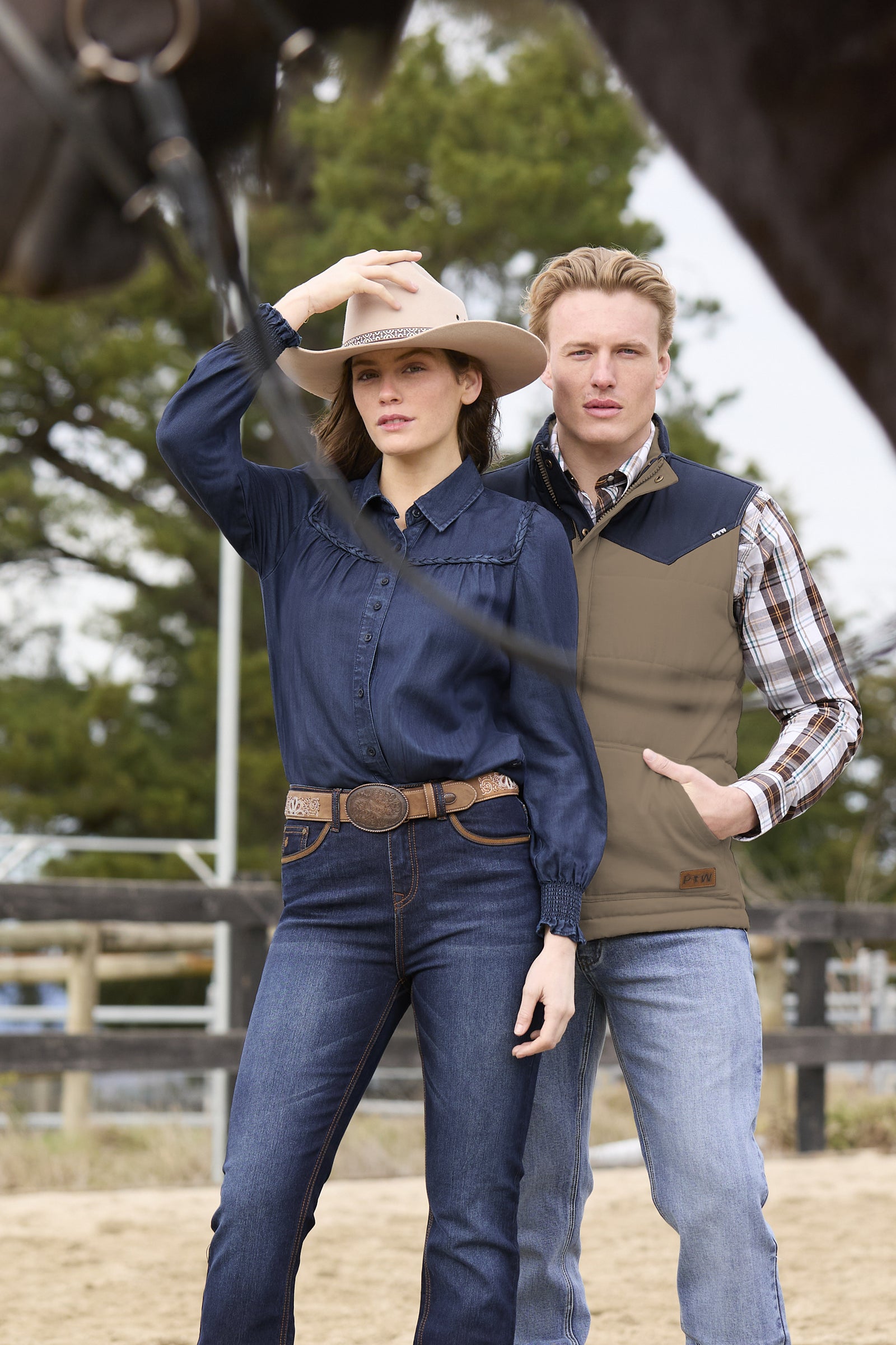 Two people in outdoor attire with a horse in the background