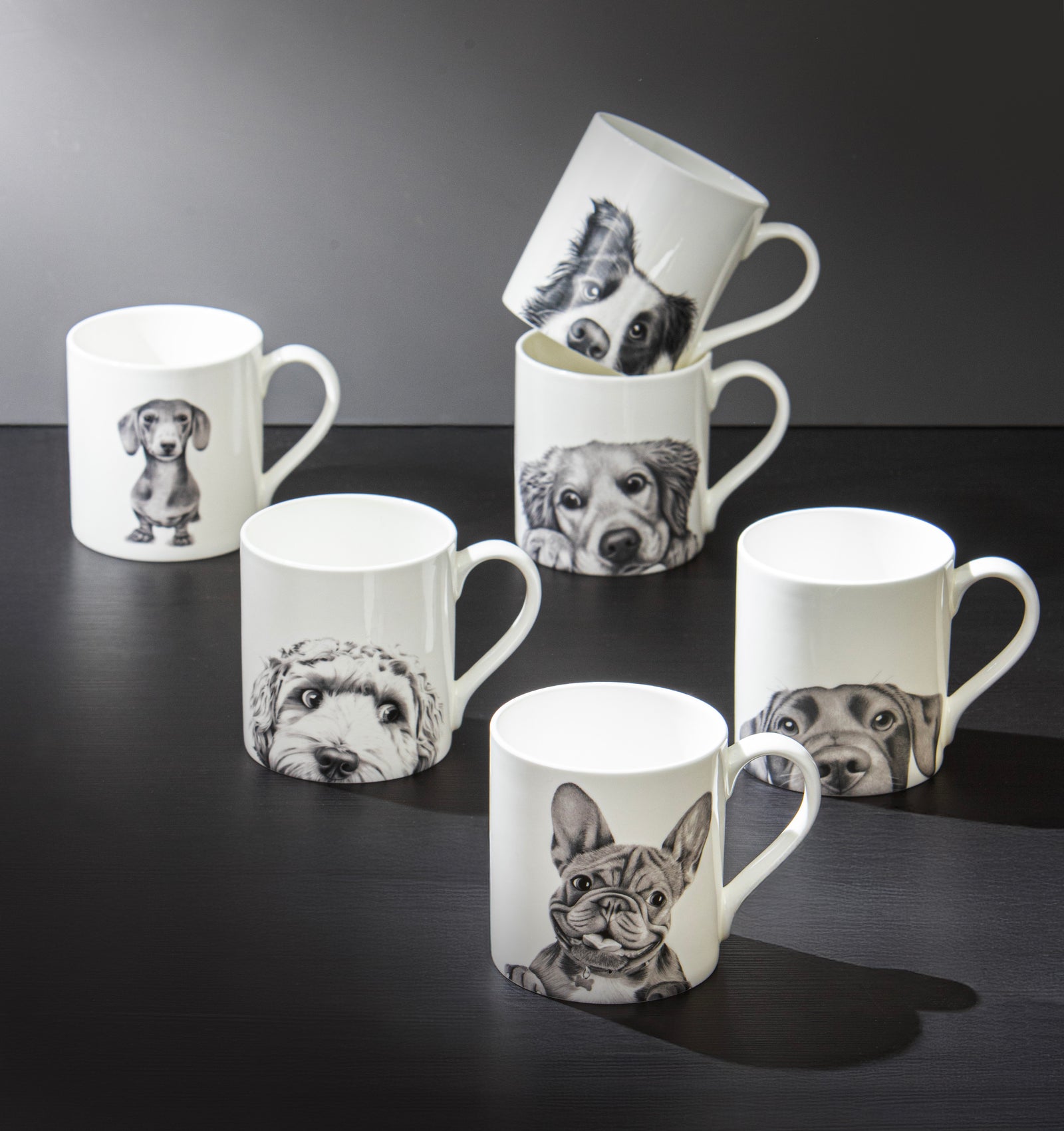 Set of mugs with black and white dog illustrations on a dark surface.