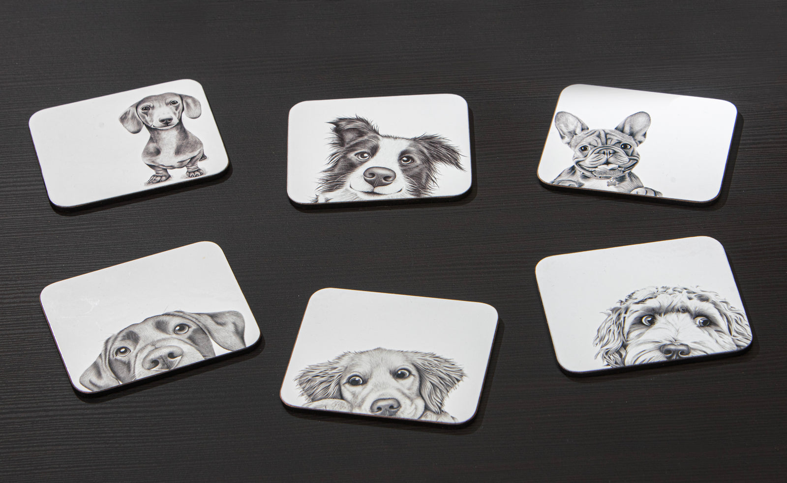 Set of six coasters with black and white illustrations of dogs on a dark surface