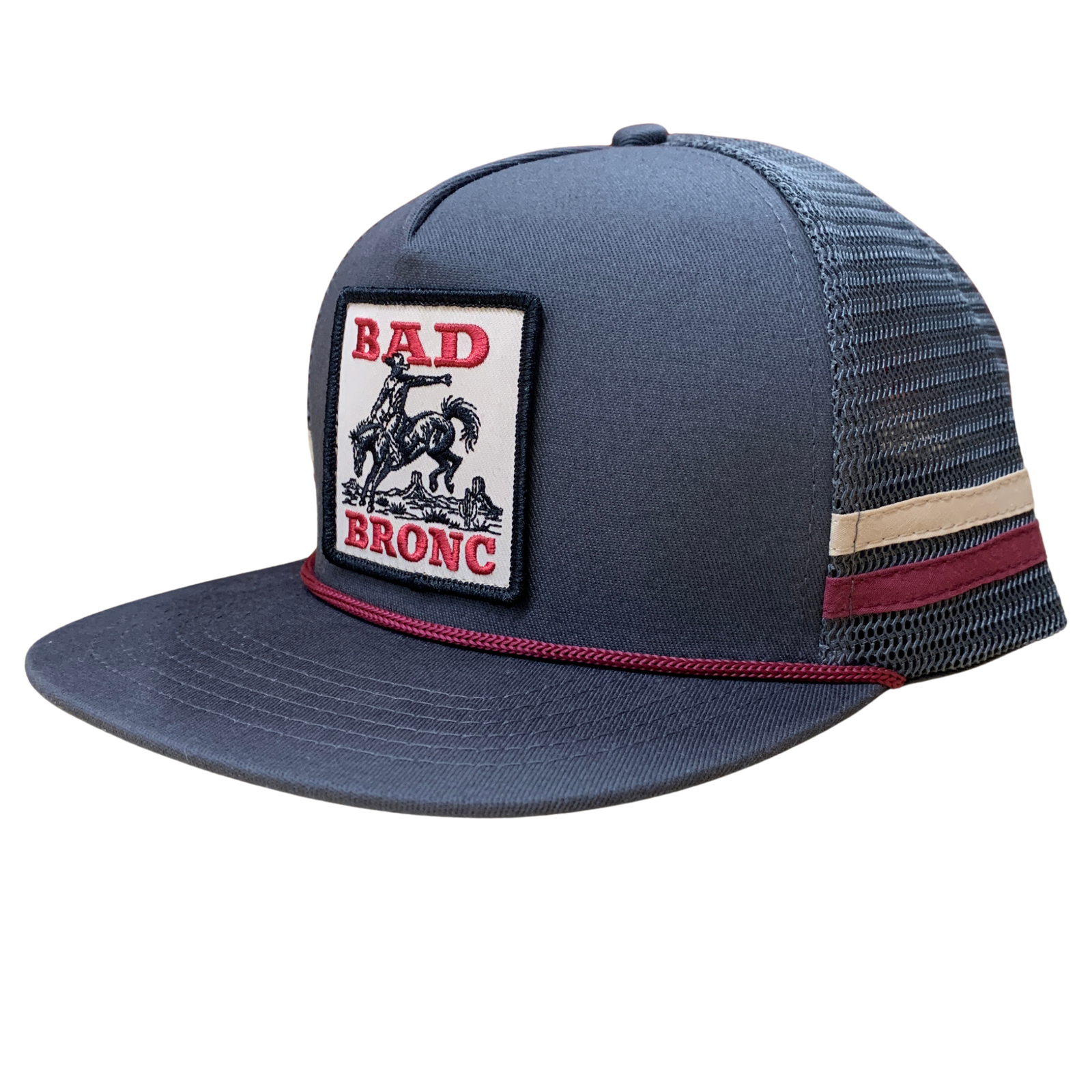 A dark slate blue trucker hat with a structured front panel, mesh back, and a rectangular 'BAD BRONC' patch on the front. The hat features a red stitched brim edge, a beige and dark red stripe on the side, and a matching red accent under the brim.