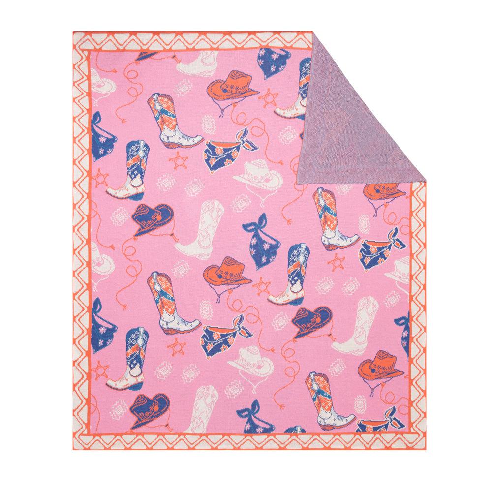 Prairie Rose Roundup Throw. A multicolored cotton throw featuring patterns of boots, hats, and bandanas on a pink background with a lasso-like border.