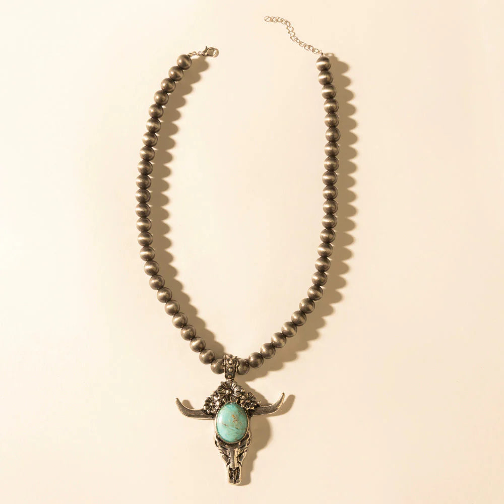 Necklace with bull head pendant and turquoise stone on a beige background