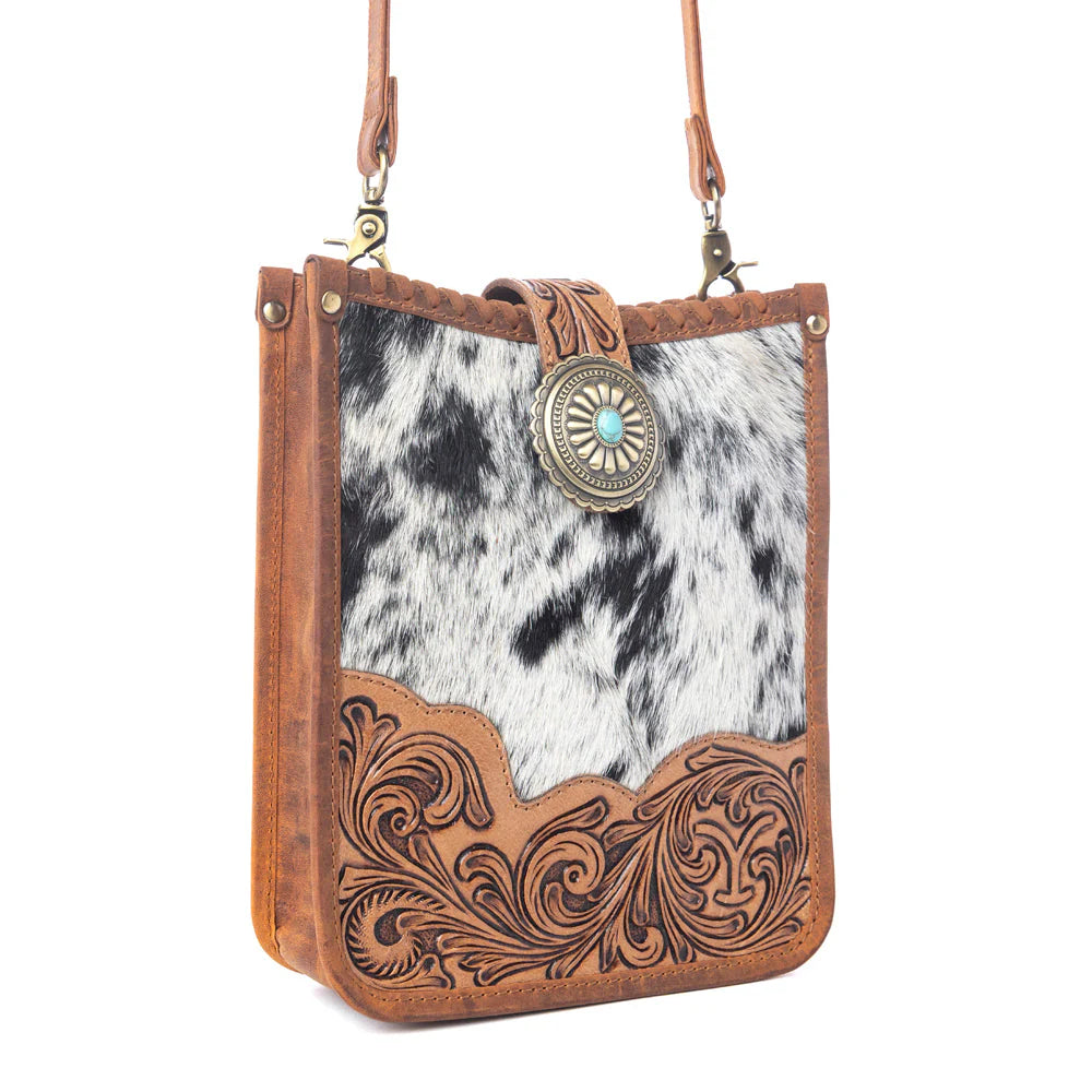Brown leather crossbody bag with cowhide pattern and decorative emblem on a white background