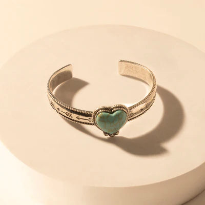 Gold bracelet with a heart-shaped green gemstone on a beige background