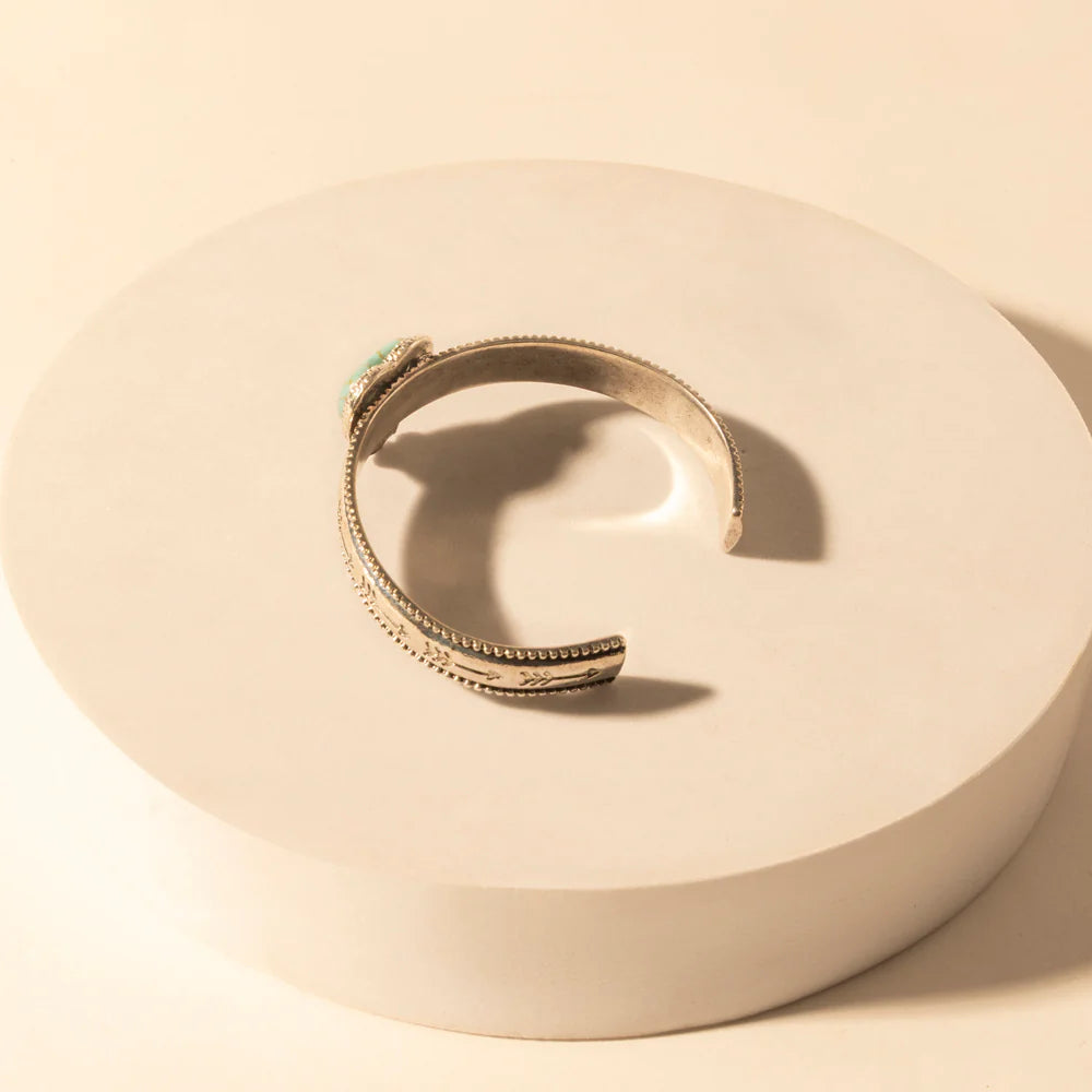 Silver ring with a green gemstone on a beige circular dish