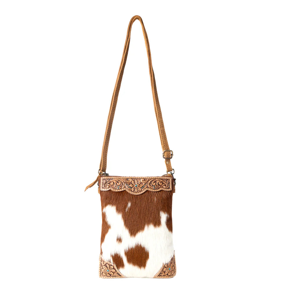 Brown and white cowhide crossbody bag with decorative trim on a white background