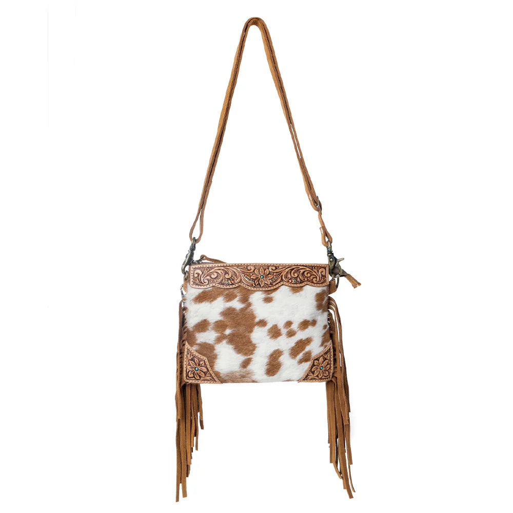 Brown and white cowhide leather handbag with fringe on a white background