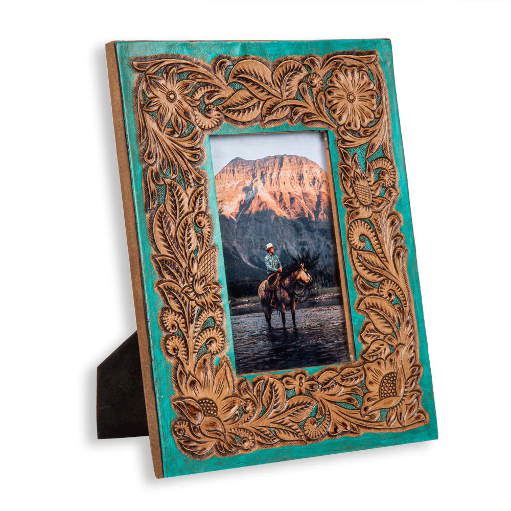 Time of Traditions Hand-Tooled Photo Frame. A hand-tooled leather photo frame with a turquoise teal background and brown detailed scrolling design, holding a picture of a person on horseback.