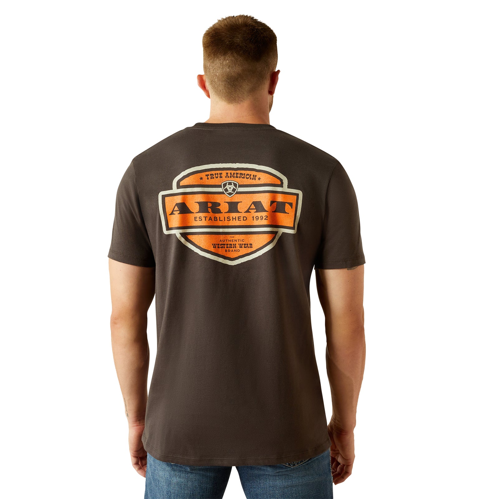 Ariat Men's Ol' Style Lockup T-Shirt. A man facing away from the camera wears a brown Ariat T-shirt with a graphic logo on the back.