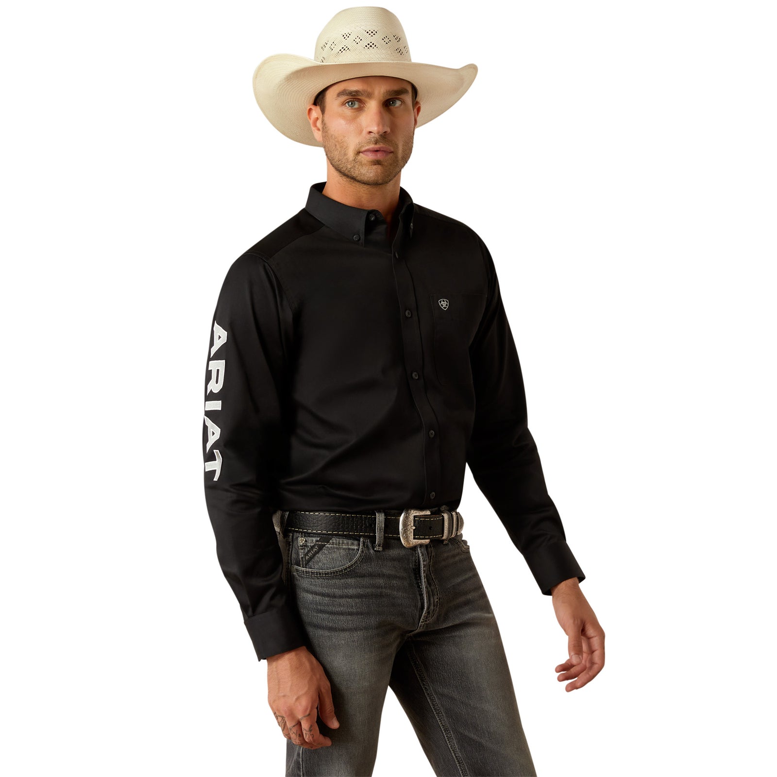 Ariat Men's Team Logo Twill L/S Western Shirt. Man wearing a black Ariat shirt, gray jeans, and a cowboy hat on a white background