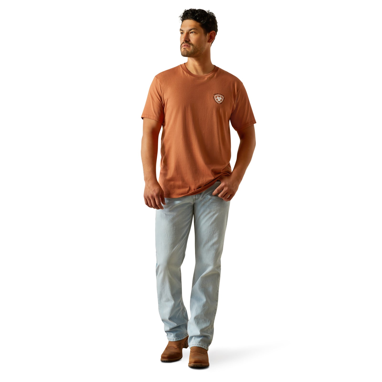 Ariat Men's Loft Simple Seal T-Shirt. Man wearing an orange t-shirt and light blue jeans on a white background